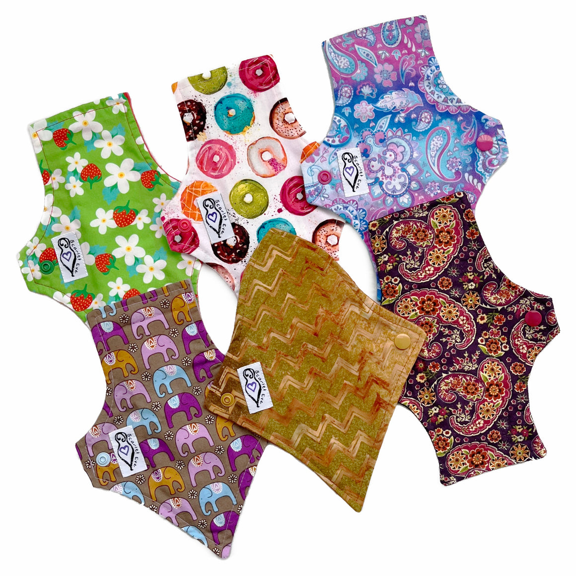 A set of six assorted panty liners with various colorful patterns, against a white background. Some Pads are squared at the top and one is curved. Some Pads are flared at the bottom and some are tapered.