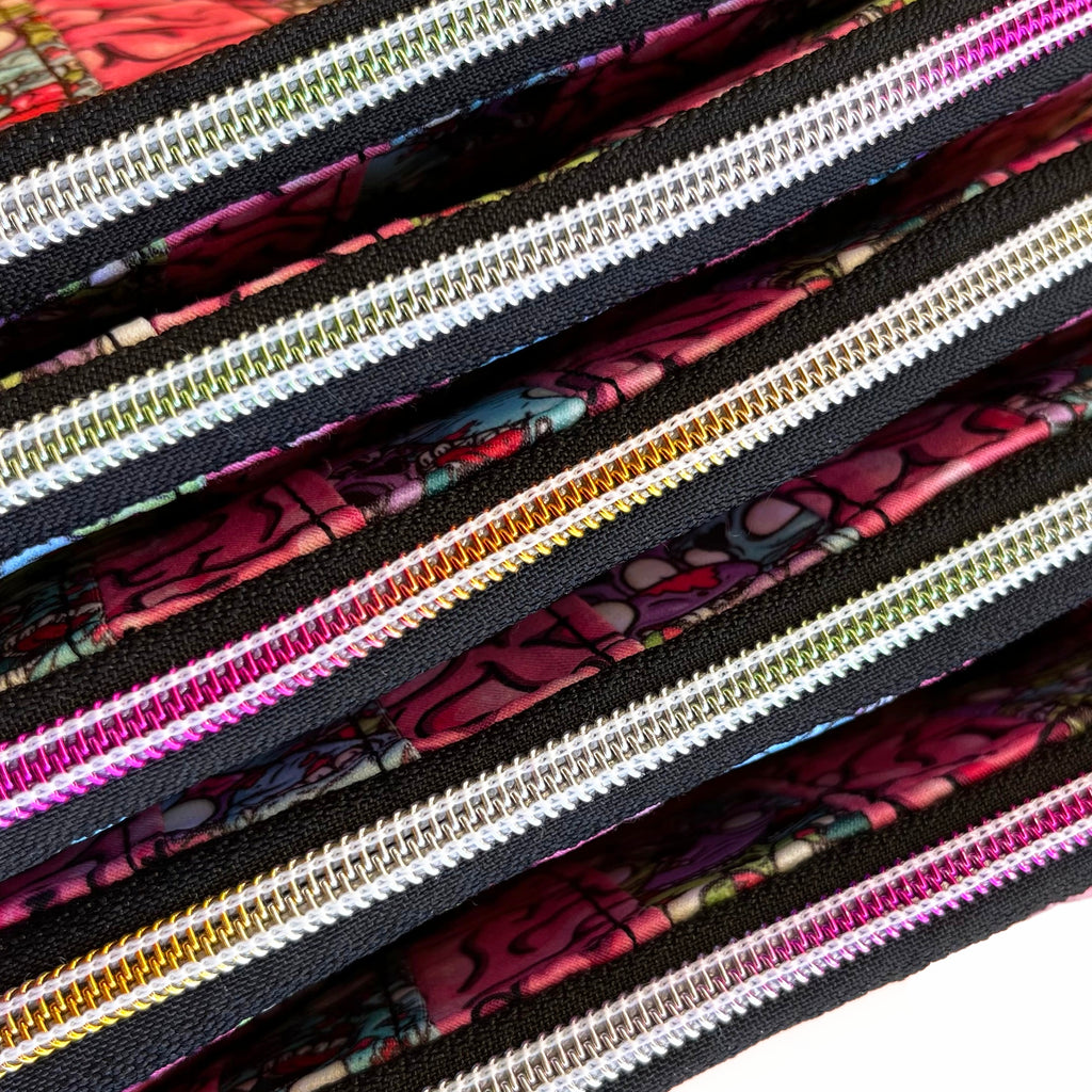 A close up of 5 variegated rainbow zippers with a small amount of multicoloured zombies and brains fabric visible.