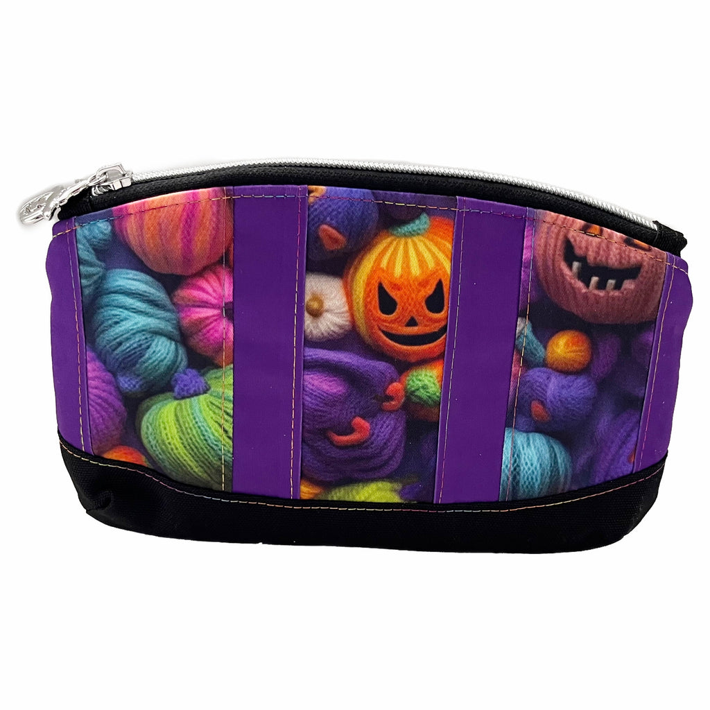 A zippered pouch with stripes of multicoloured yarn pumpkins and purple PUL fabric, with a black canvas  base. A black zipper with a silver pumpkin zip pull.