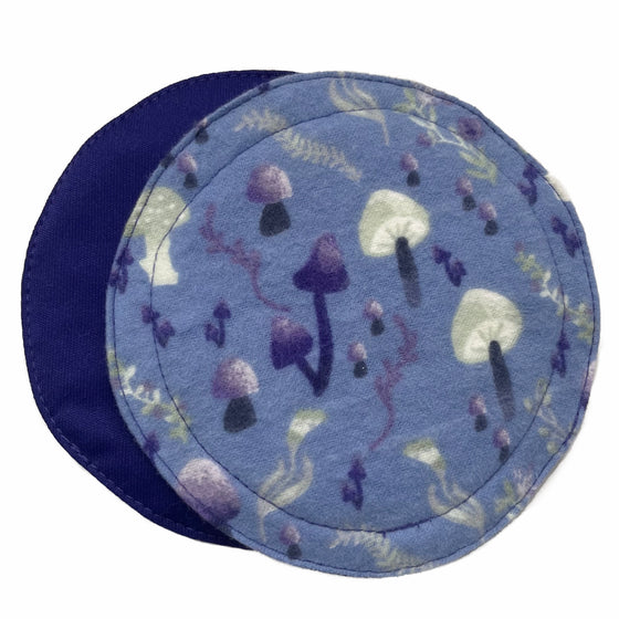 Two reusable breast pads against a white background. The pad on top is made from light blue cotton flannel with purple and grey mushrooms. The pad on the bottom is made from purple PUL fabric.