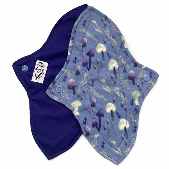Two reusable menstrual pads with a contoured shape against a white background. The pad on top is made from blue cotton flannel with purple and grey mushrooms. The pad on the bottom is made from purple PUL fabric and has a white "Scarlet Eve" label.