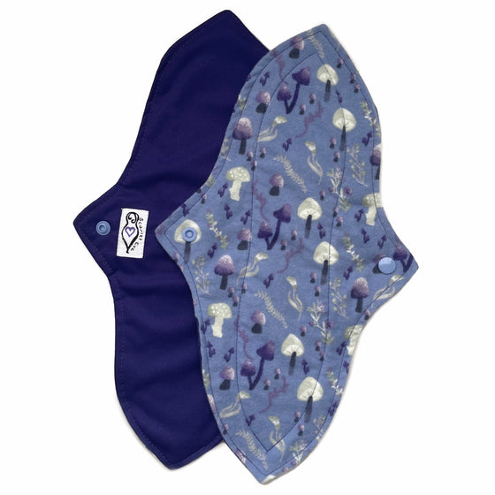 Two reusable menstrual pads with a contoured shape against a white background. The pad on top is made from blue cotton flannel with purple and grey mushrooms. The pad on the bottom is made from purple PUL fabric and has a white "Scarlet Eve" label.