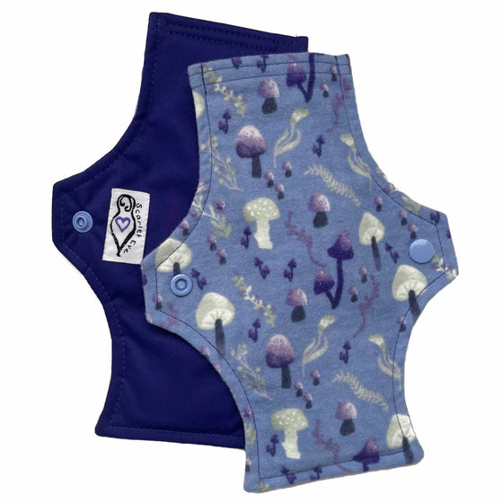 Two reusable menstrual pads with squared top and flared bottom shape against a white background. The pad on top is made from blue cotton flannel with purple and grey mushrooms. The pad on the bottom is made from purple PUL fabric and has a white "Scarlet Eve" label.