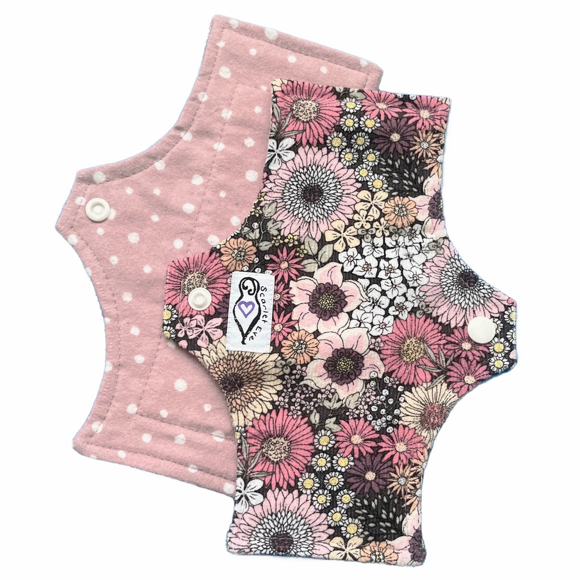 Two reusable panty liners against a white background. The top Pad is made from pink floral corduroy with a white 'Scarlet Eve' label. The Pad underneath is made from dusty pink flannel with small white spots.