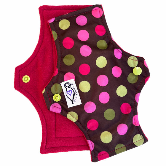 Two reusable menstrual pads with squared top and flared bottom shape, against a white background. The pad on top is made from chocolate brown PUL fabric with pink and green spots . The pad on the bottom is made from raspberry red microfleece fabric.