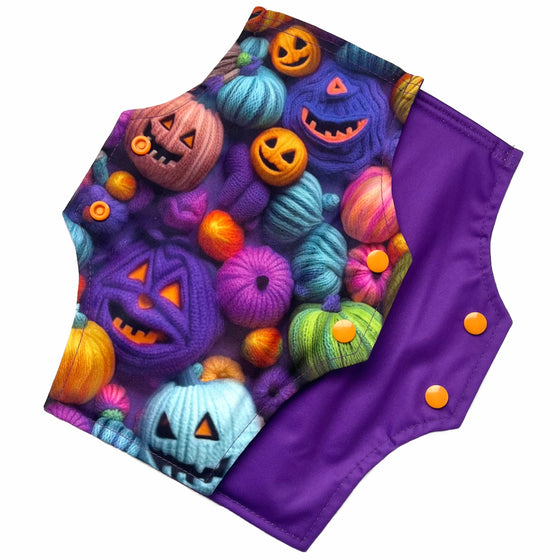 Two reusable menstrual pads with squared top and flared bottom shape against a white background. The pad on top is made from purple woven cotton with orange, purple, green and blue pumpkins made from yarn. The pad on the bottom is made from purple PUL fabric and has a white "Scarlet Eve" label.