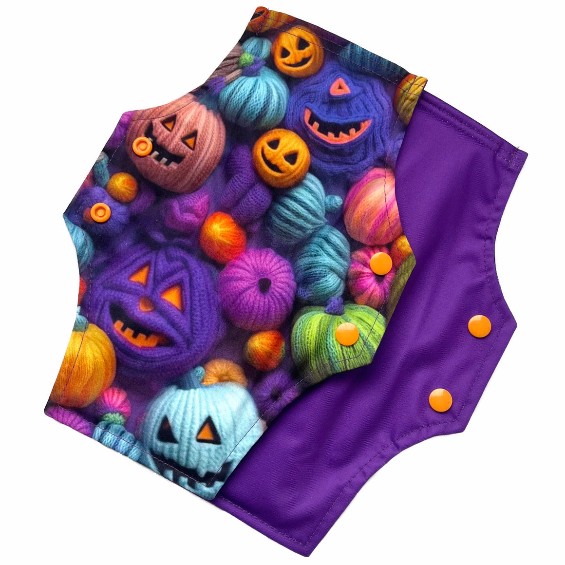 Two reusable menstrual pads with squared top and flared bottom shape against a white background. The pad on top is made from purple woven cotton with orange, purple, green and blue pumpkins made from yarn. The pad on the bottom is made from purple PUL fabric and has a white "Scarlet Eve" label.