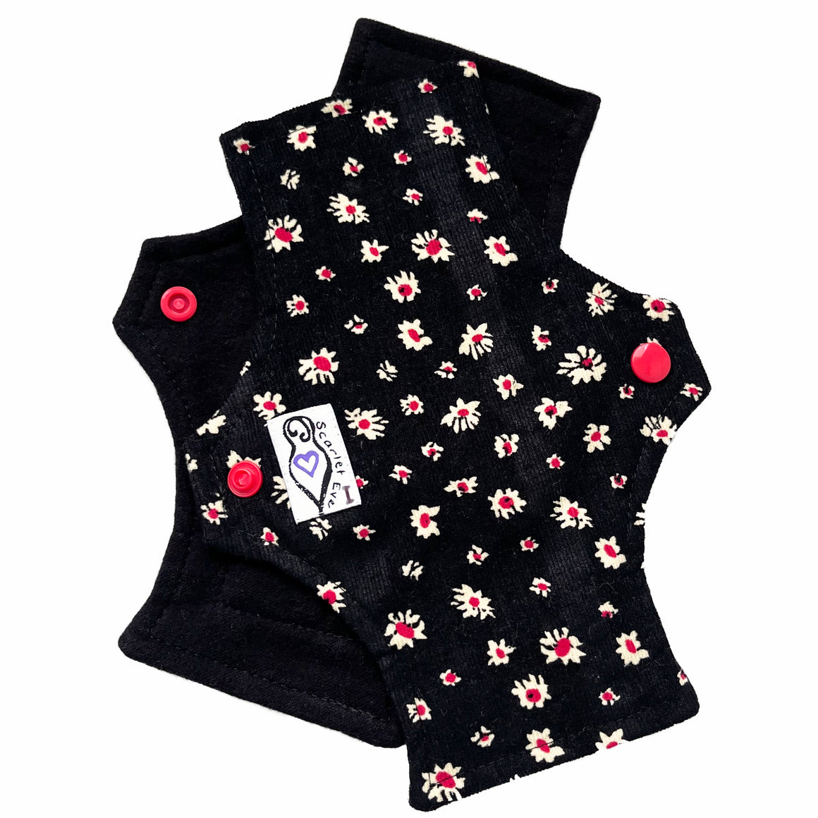 Two reusable panty liners against a white background. The pad on top is made from white and red daisies on black corduroy, and has a white 'Scarlet Eve' label with an I on it. The pad on the bottom is made from black flannel fabric.