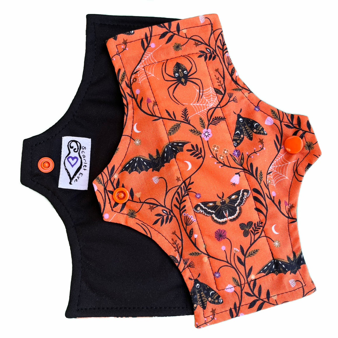 Two reusable mesntrual pads with squared top and flared bottom shape against a white background. The pad on top is made from orange woven cotton with black moths, bats and leaves. The pad on the bottom is made from black PUL fabric and has a white "Scarlet Eve" label.