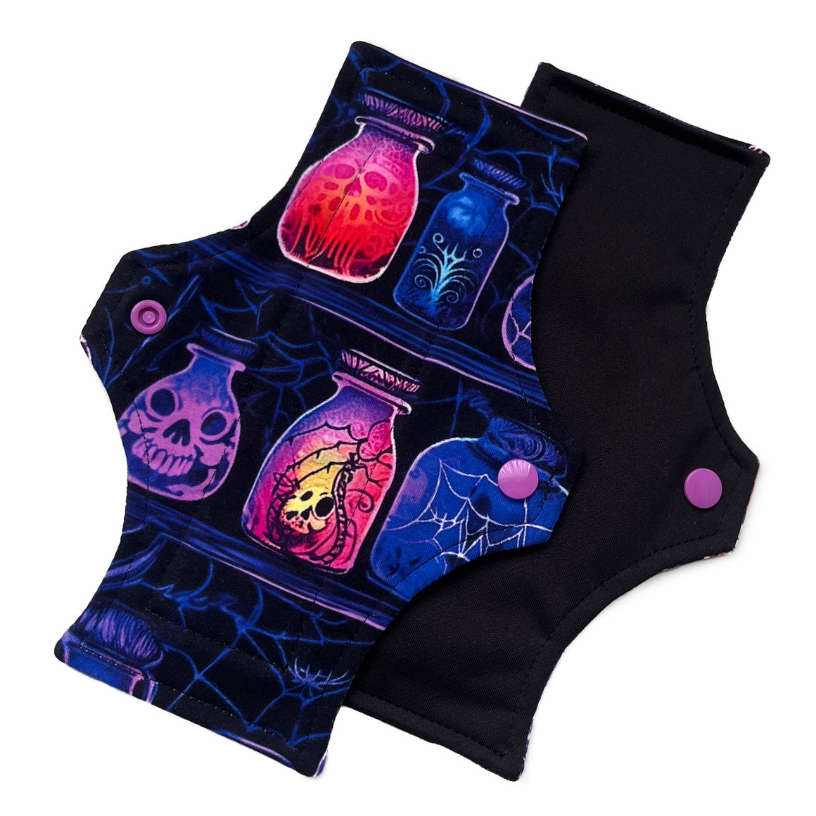 Two reusable menstrual pads with a squared top and flared bottom shape against a white background. The pad on top is made from black cotton Lycra with potion bottles in neon colours. The pad on the bottom is made from black PUL fabric and has a white "Scarlet Eve" label.
