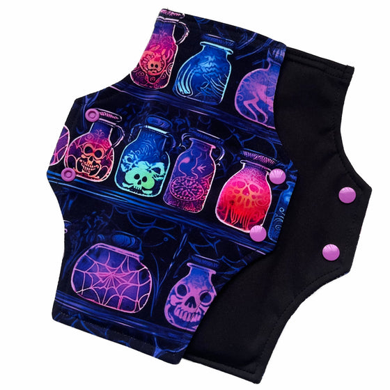 Two reusable menstrual pads with a squared top and flared bottom shape against a white background. The pad on top is made from black cotton Lycra with potion bottles in neon colours. The pad on the bottom is made from black PUL fabric and has a white "Scarlet Eve" label.