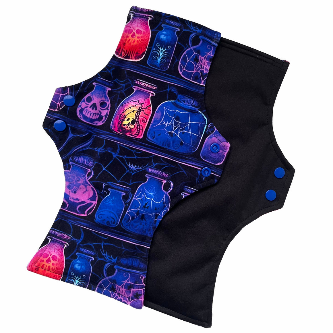 Two reusable menstrual pads with a squared top and flared bottom shape against a white background. The pad on top is made from black cotton Lycra with potion bottles in neon colours. The pad on the bottom is made from black PUL fabric and has a white "Scarlet Eve" label.