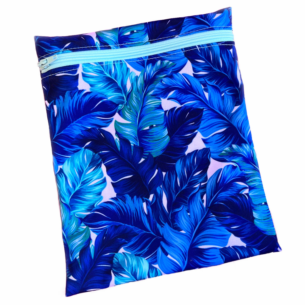 A rectangular zippered pouch against a white background. The wet bag is made from printed PUL fabric with blue and turquoise monstera leaves on a pale pink background. A mint coloured zip runs along the pouch towards the top.