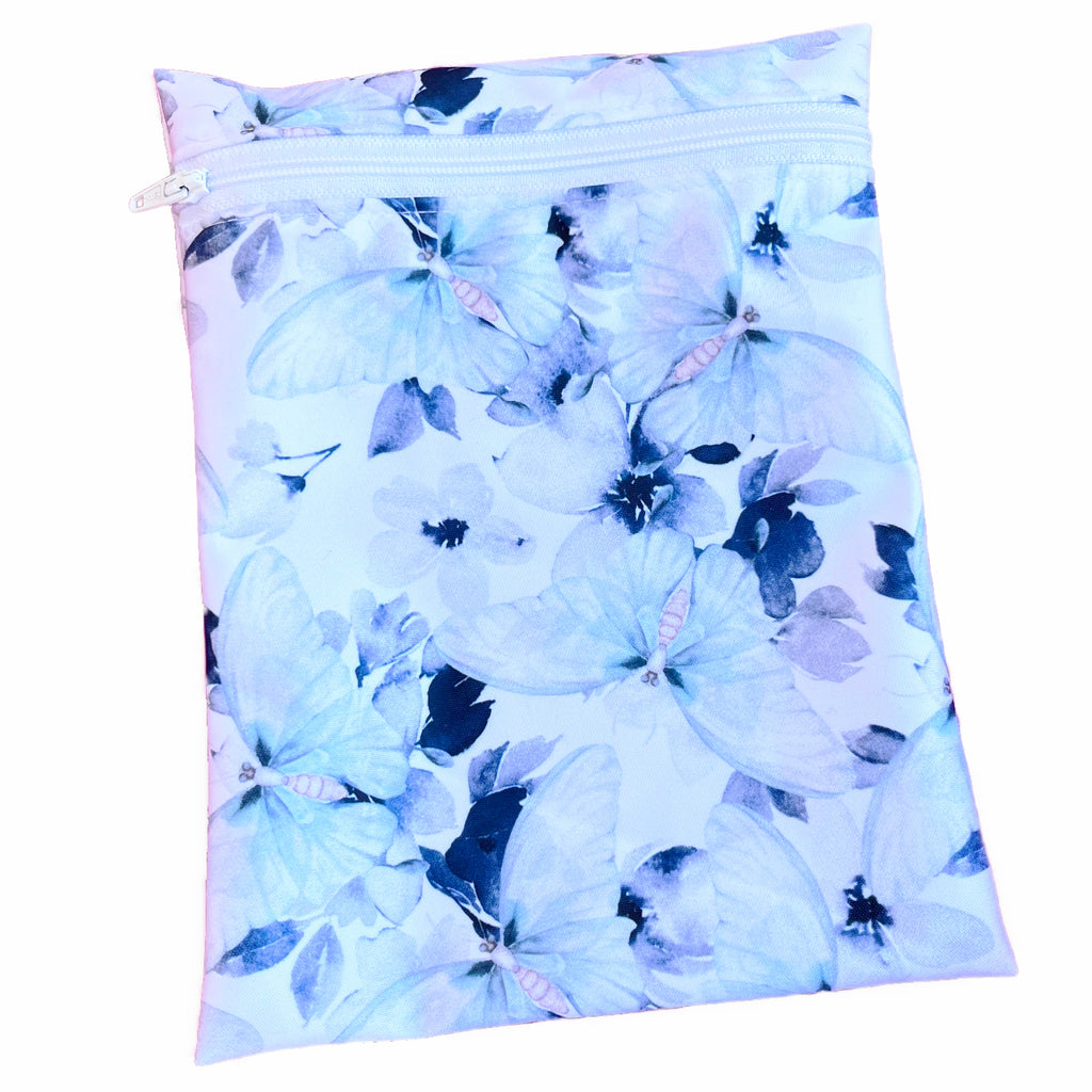 A rectangular zippered pouch against a white background. The wet bag is made from printed PUL fabric with large watercolour butterflies on white. A white coloured zip runs along the pouch towards the top.