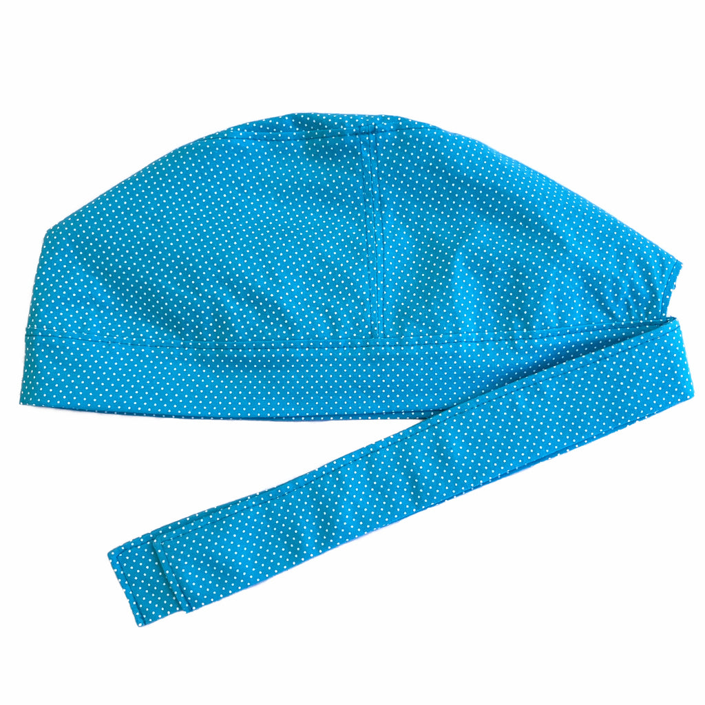 A pink and white scrub cap against a white background. The cap, bottom band and ties are made from aqua blue woven cotton with very small white dots.