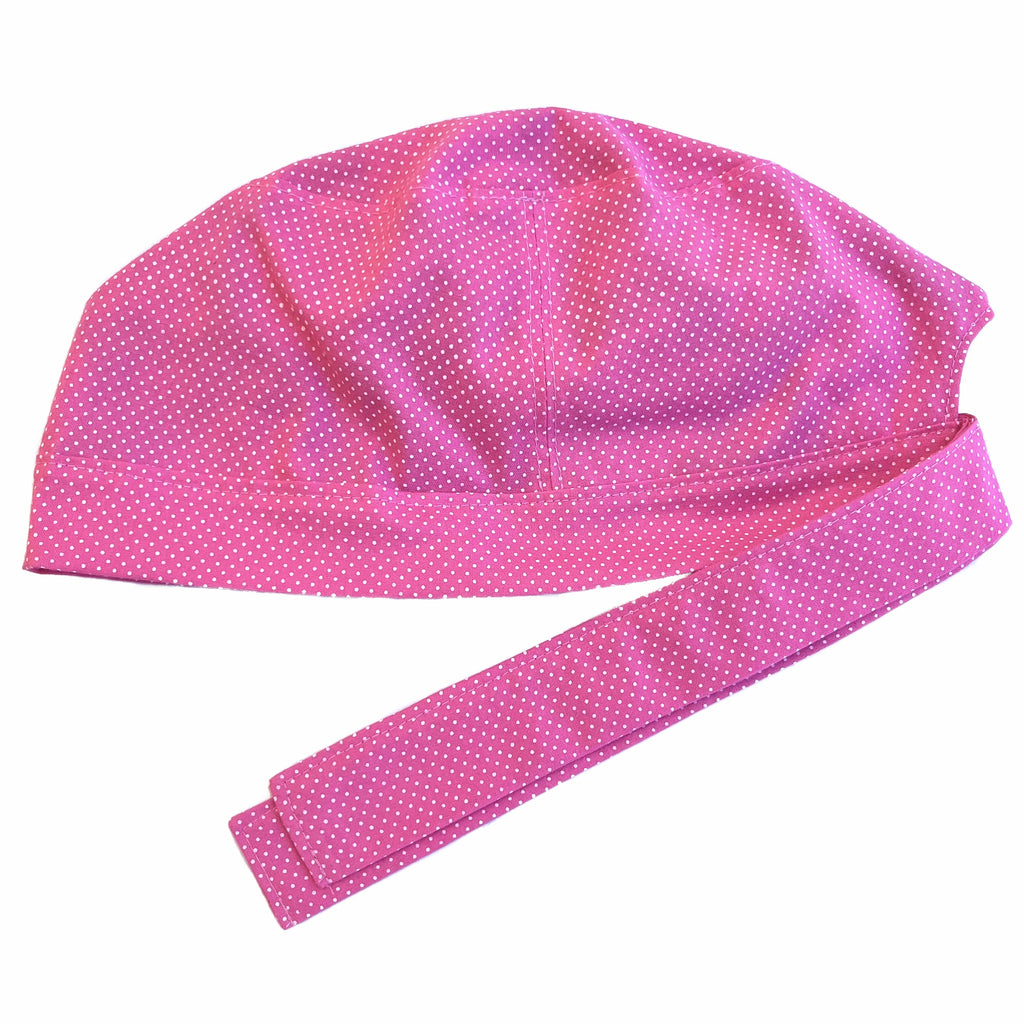 A pink and white scrub cap against a white background. The cap, bottom band and ties are made from pink woven cotton with very small white dots.