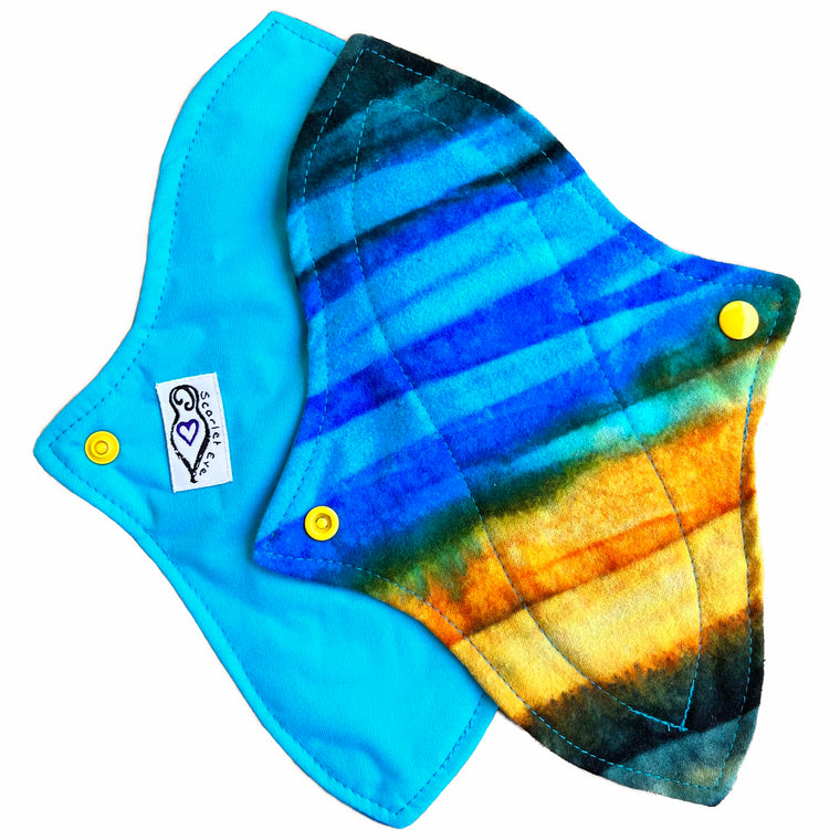 Two reusable menstrual pads with a contoured shape against a white background. The pad on top is made from flannel fabric with batik striations of yellow, aqua and indigo. The pad on the bottom is made from aqua blue PUL fabric.