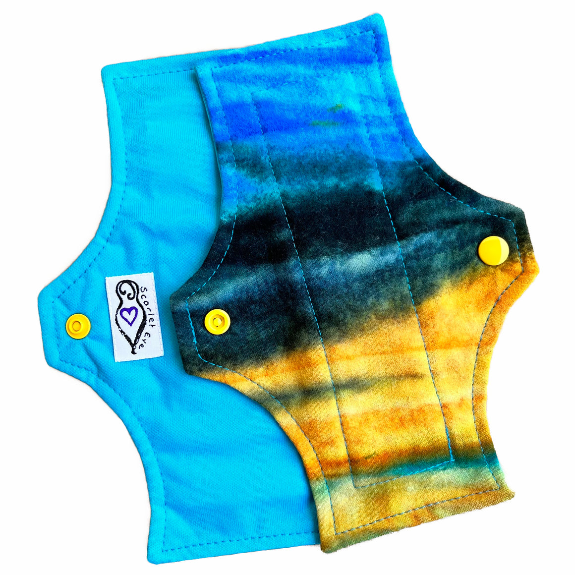 Two reusable menstrual pads with squared top and flared bottom shape against a white background. The pad on top is made from flannel fabric with batik striations of yellow, aqua and indigo. The pad on the bottom is made from aqua blue PUL fabric.