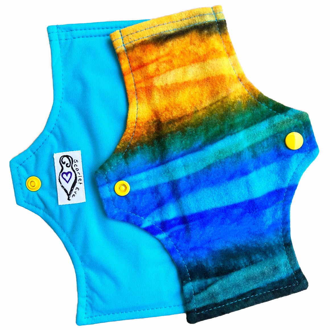 Two reusable menstrual pads with squared top and flared bottom shape against a white background. The pad on top is made from flannel fabric with batik striations of yellow, aqua and indigo. The pad on the bottom is made from aqua blue PUL fabric.