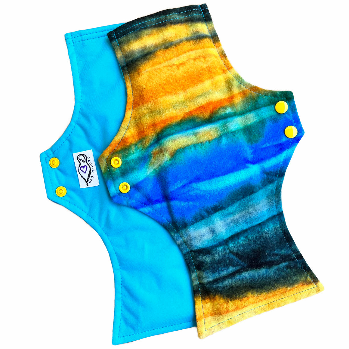 Two reusable menstrual pads with squared top and flared bottom shape against a white background. The pad on top is made from flannel fabric with batik striations of yellow, aqua and indigo. The pad on the bottom is made from aqua blue PUL fabric.
