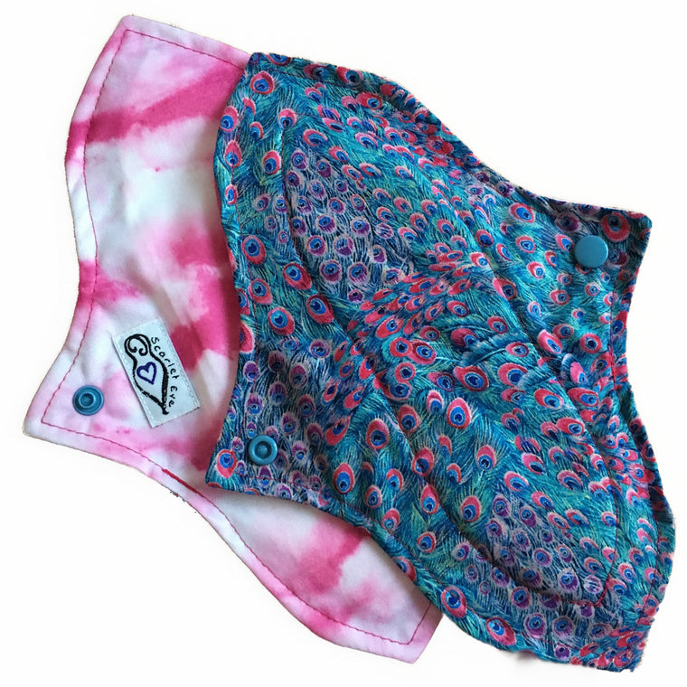 Two reusable menstrual pads with a contoured shape against a white background. The pad on top is made from teal woven cotton with pink, purple and turquoise peacock feather print. The pad on the bottom is made from white and pink clouds PUL fabric, and has a white "Scarlet Eve" label.