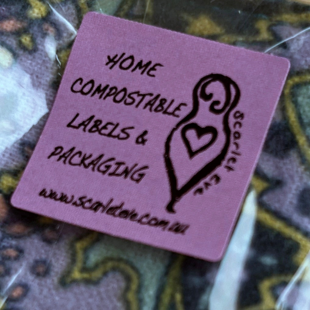 A close up of a clear bag with colourful square face wipes inside. The bag has a purple label with  black text that reads "HOME COMPOSTABLE LABELS & PACKAGING" with the Scarlet Eve logo and website url.