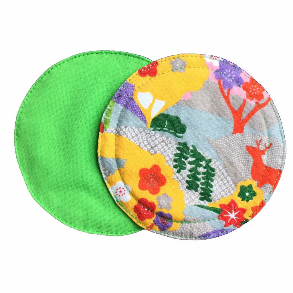 Two reusable nursing pads against a white background. The breast pad on top is made from cotton jersey fabric with a bright forest print. The breast pad on the bottom is made from lime PUL fabric.