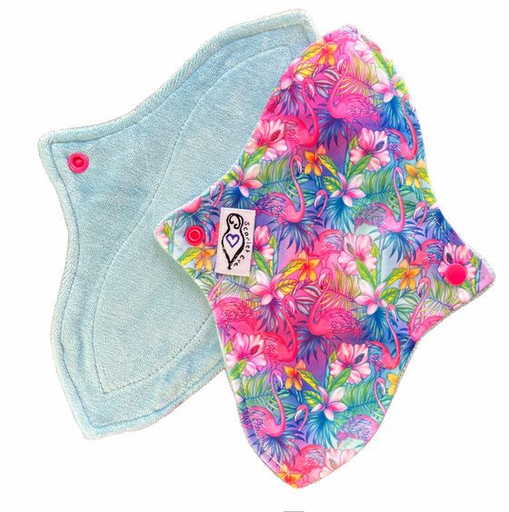 Two reusable menstrual pads with a contoured shape against a white background. The pad on top is made from  light blue fabric with a bright, tropical flamingos print and has a white "Scarlet Eve" label. The pad on the bottom is made from light blue bamboo velour fabric.