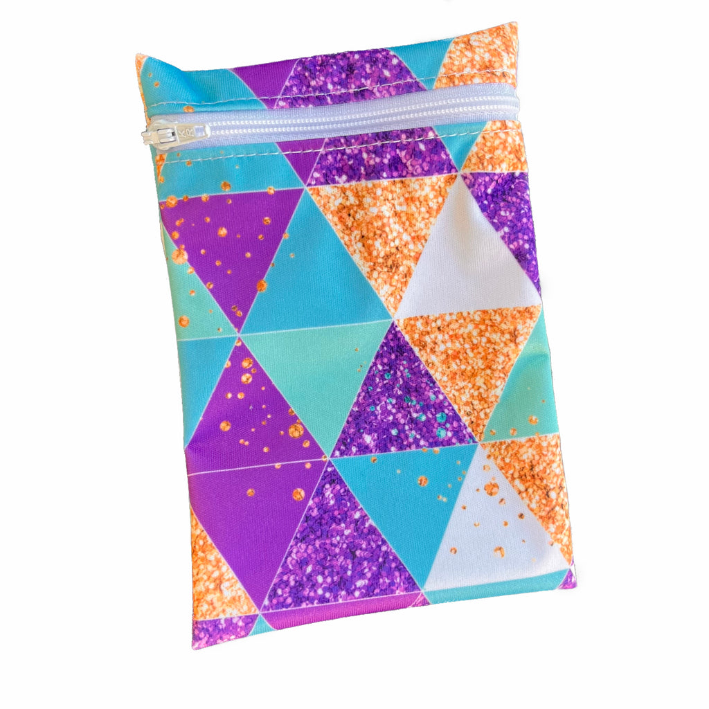 A rectangular zippered pouch against a white background. The wet bag is made from printed PUL fabric with triangles in turquoise, purple, white and gold. A white coloured zip runs along the pouch towards the top.