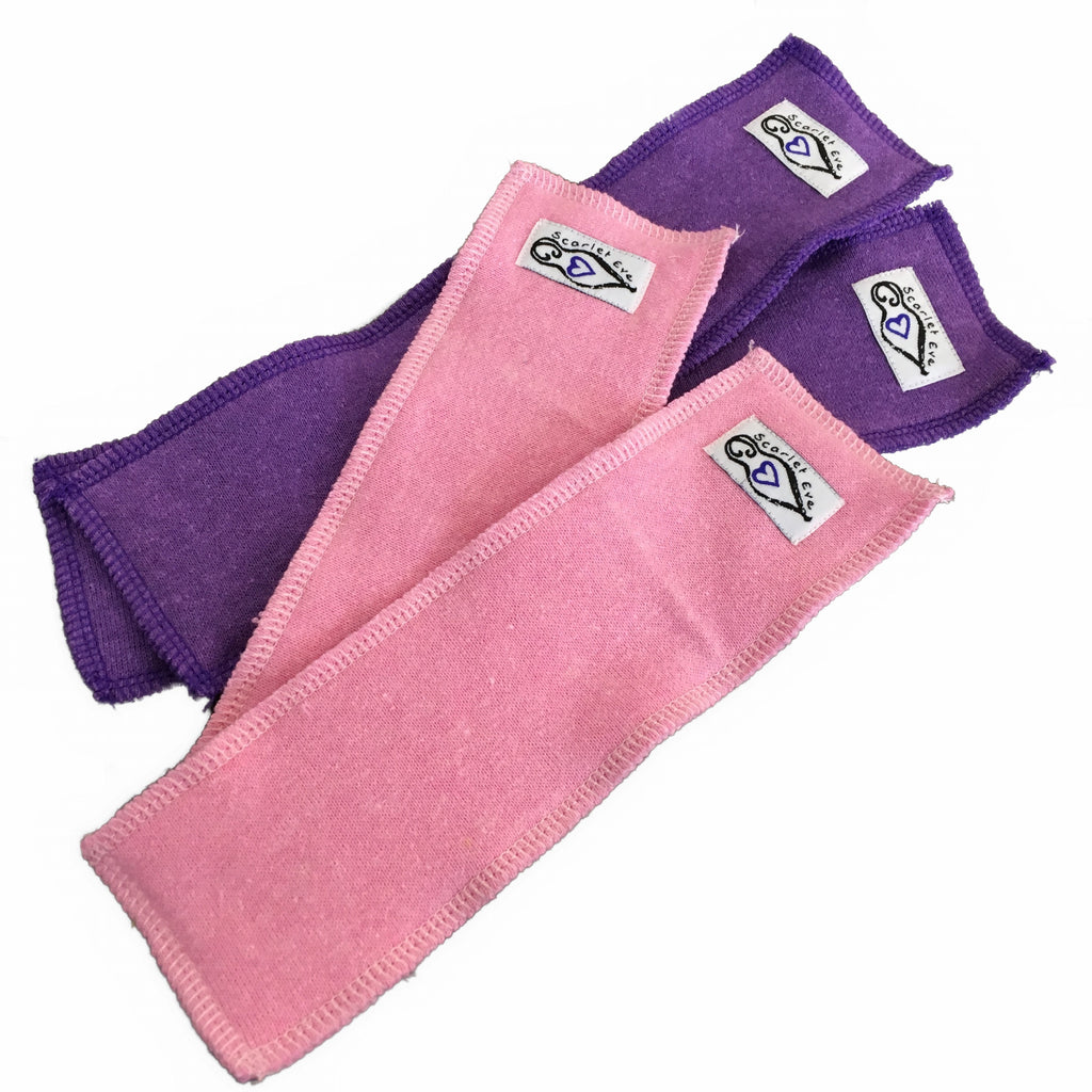 Four rectangular fleece boosters with white "Scarlet Eve" labels, against a white background. The two larger boosters underneath are purple fleece with purple overlocking, and the two smaller boosters on top are light pink fleece with light pink overlocking.