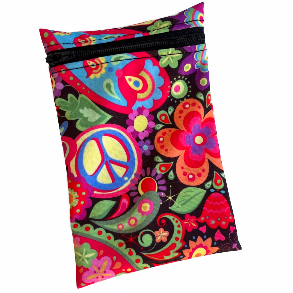 A rectangular zippered pouch against a white background. The wet bag is made from black PUL fabric with a bright, hippy themed print with paisley and peace signs. A black coloured zip runs along the pouch towards the top.