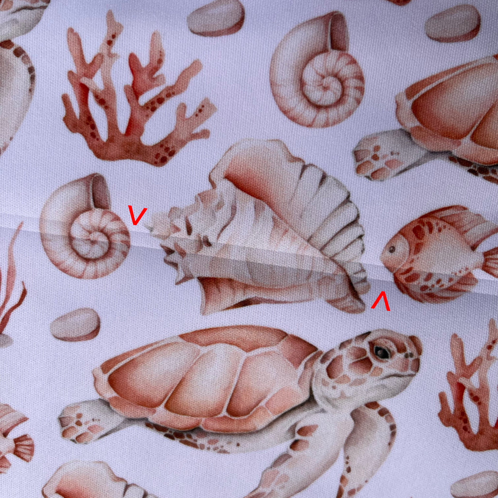 A close up of white PUL fabric with sea creatures print. Red arrows point to indented fault lines running across the fabric.