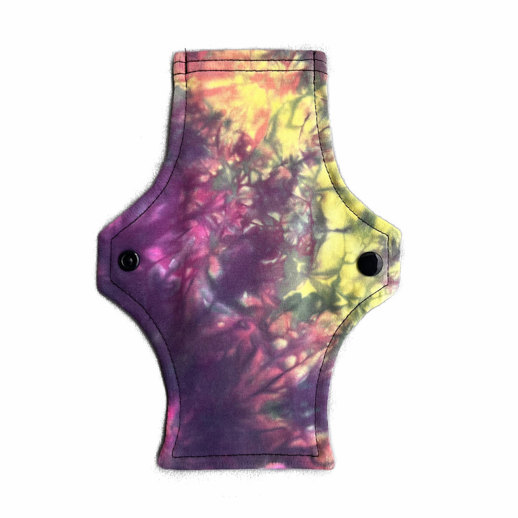 A reusable cloth menstrual pad with a squared top and flared bottom shape, against a white background. The pad tie dye cotton lycra fabric in pastel pink, yellow and black shades.