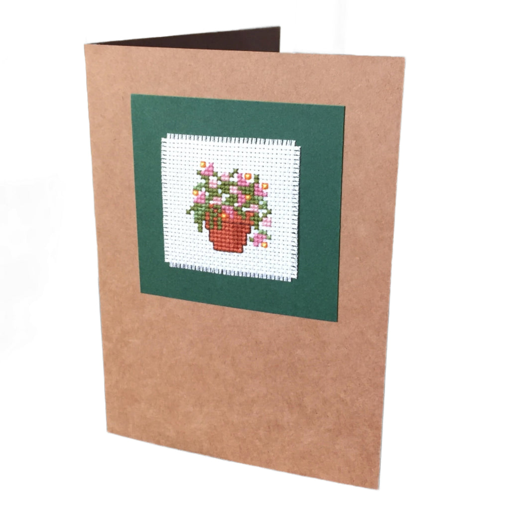 A handcrafted cardboard gift card with a cross stitch design featuring a pot of pink flowers, mounted on a brown card.