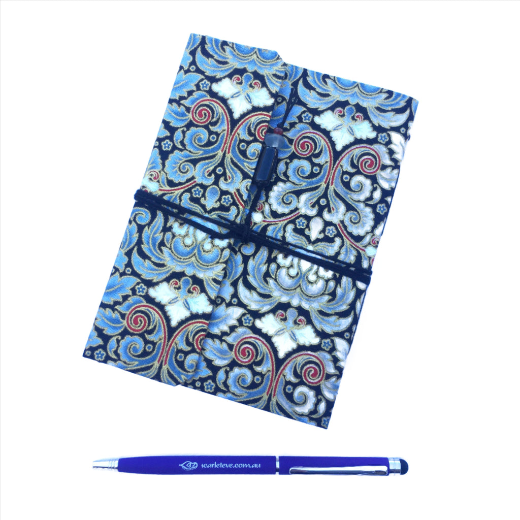 A fabric covered journal and pen, against a white background. The journal is covered in a blue and red filigree print fabric. The pen at the bottom is purple and silver, with the Scarlet Eve logo and website url along the barrel. 