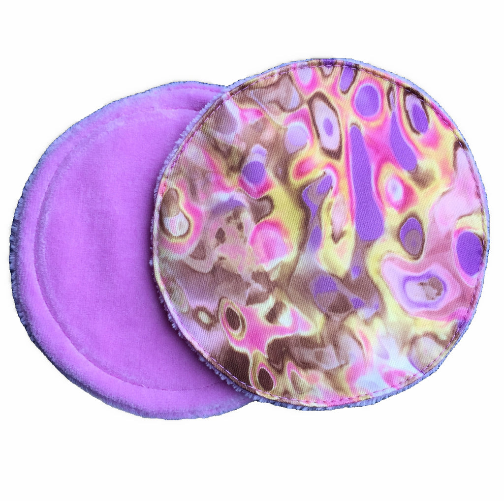 Two reusable nursing pads against a white background. The breast pad on top is made from PUL fabric with an abstract pink, purple and brown print. The breast pad on the bottom is made from pink velour fabric.