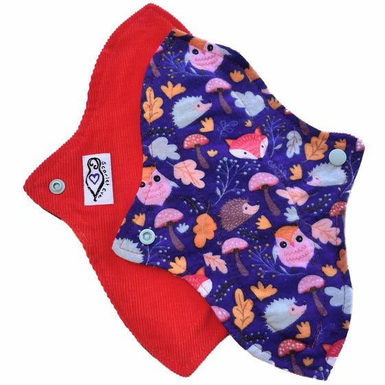 Two reusable menstrual pads with a contoured shape, against a white background. The pad on top is made from dark blue flannel with cartoon forest animals and plants. The pad on the bottom is made from dark orange corduroy and has a white "Scarlet Eve" label.