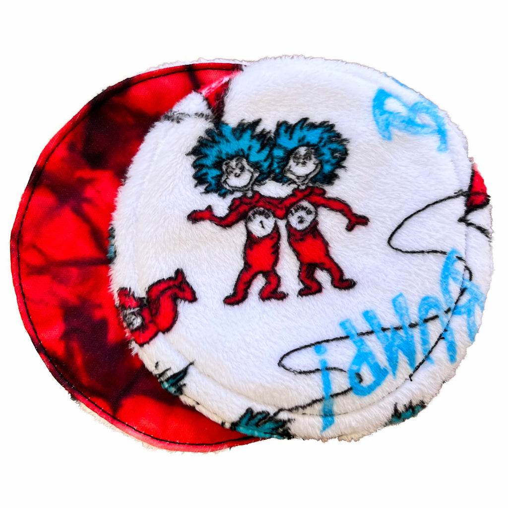 Two reusable nursing pads against a white background. The breast pad on top is made from white Minky with Thing 1 and 2 characters and blue "BUMP!" text. The breast pad on the bottom is made from red and black swirl PUL fabric.