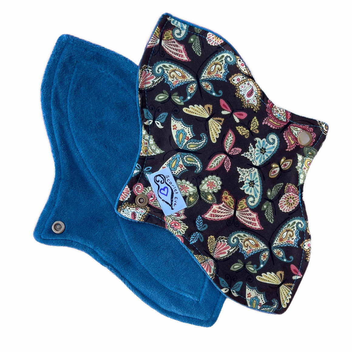 Two reusable menstrual pads with a contoured shape, against a white background. The pad on top is made from dark brown cotton fabric with pink and blue paisley butterflies print, and has a white "Scarlet Eve" label. The pad on the bottom is made from jade green velour fabric.