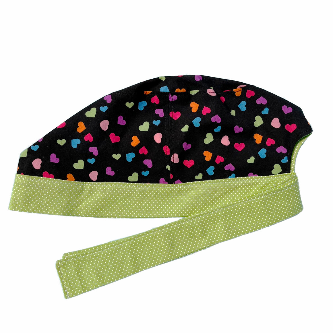 A black and green scrub cap against a white background. The main part of the cap is made from black woven cotton with small multicoloured hearts. The bottom band and ties are made from apple green woven cotton with very small white dots.