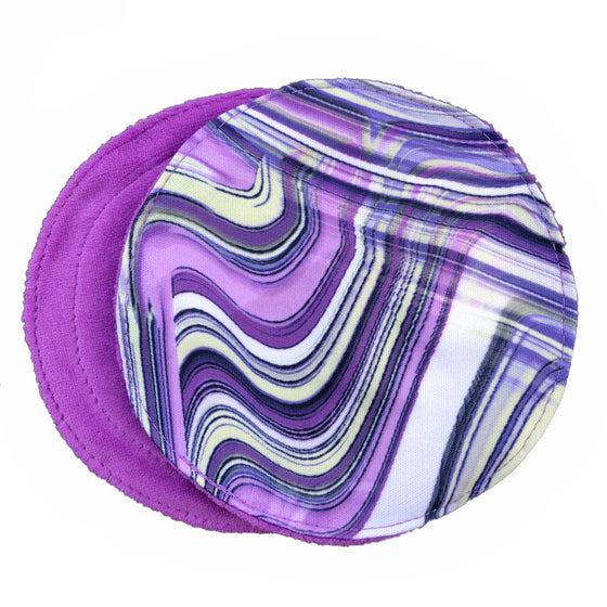 Two reusable nursing pads against a white background. The breast pad on top is made from white PUL fabric with a violet and navy swirl pattern. The breast pad on the bottom is made from violet velour fabric.