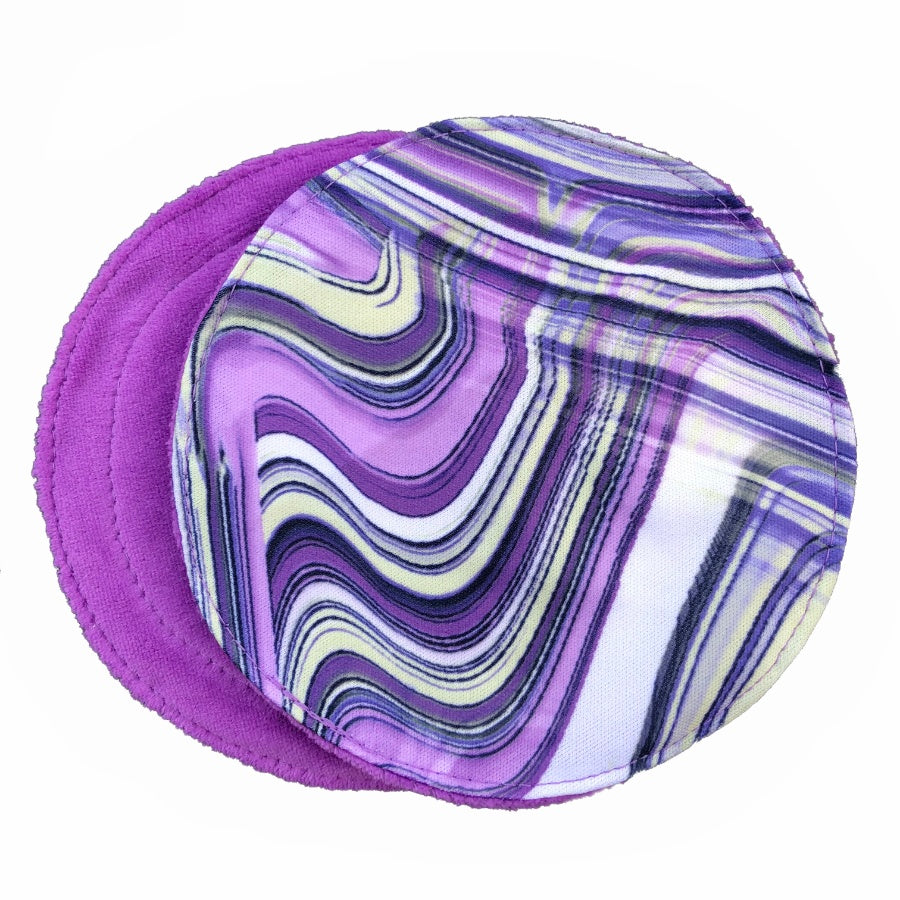 Two reusable nursing pads against a white background. The breast pad on top is made from white PUL fabric with a violet and navy swirl pattern. The breast pad on the bottom is made from violet velour fabric.