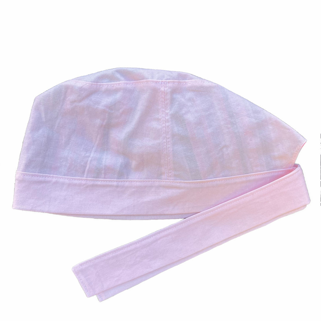 A light pink scrub cap against a white background. The cap, bottom band and ties are made from light pink woven cotton.