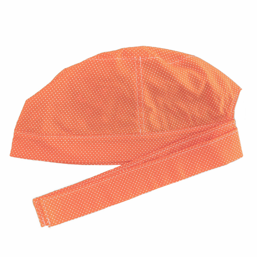 An orange and white scrub cap against a white background. The cap, bottom band and ties are made from orange woven cotton with very small white dots.