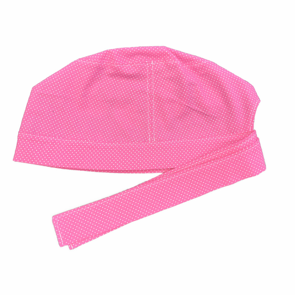 A pink and white scrub cap against a white background. The cap, bottom band and ties are made from pink woven cotton with very small white dots.